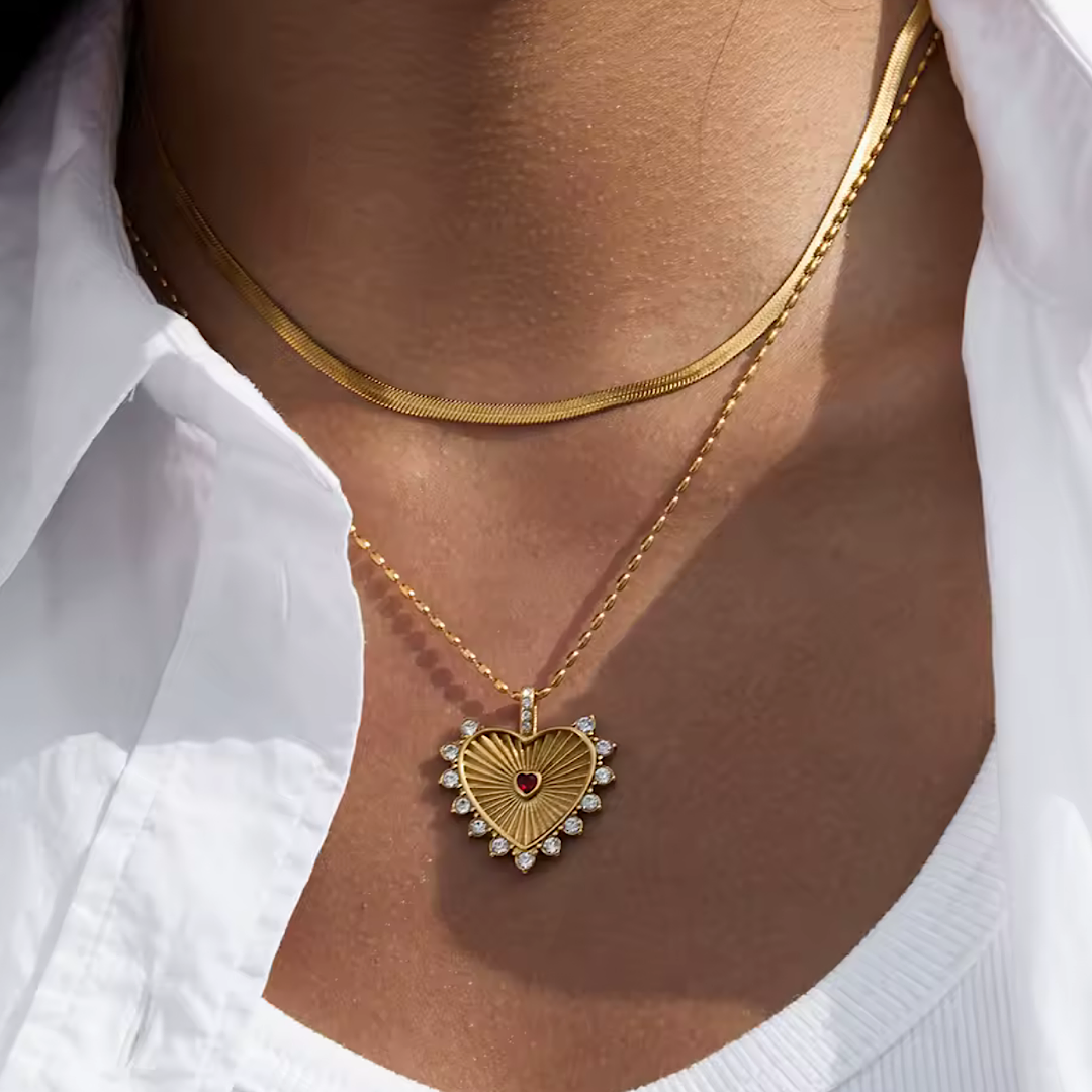 Gold heart-shaped necklace with a pendant on a person wearing a white shirt.