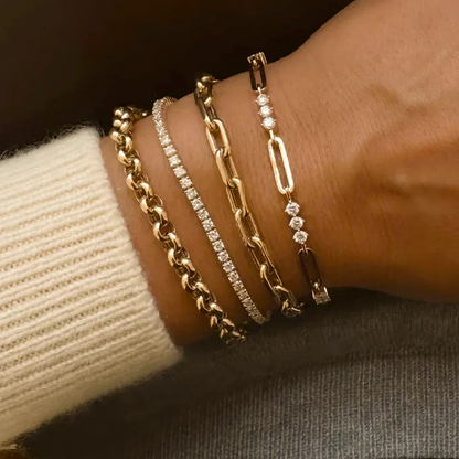 Close-up of a wrist wearing multiple gold and diamond bracelets on a neutral background