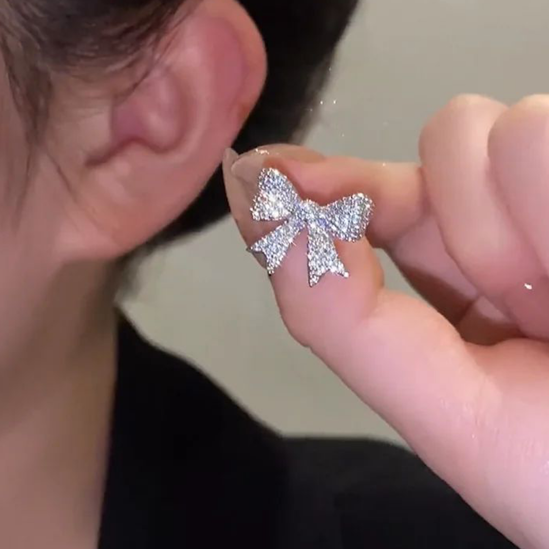 Silver bow-shaped earring held up to a person's ear.