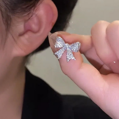 Silver bow-shaped earring held up to a person's ear.
