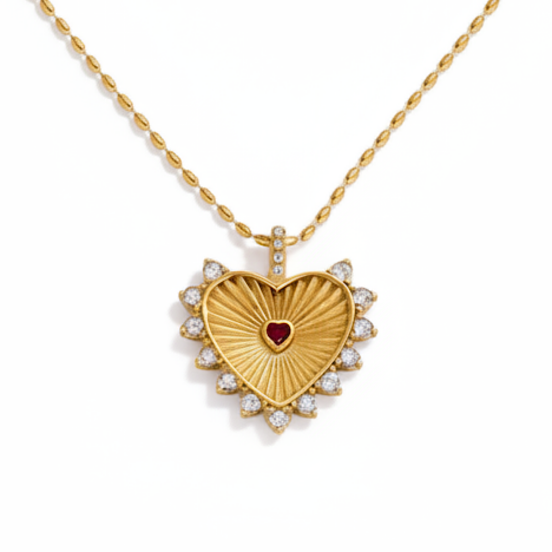 Gold heart-shaped necklace with a red gemstone center on a white background