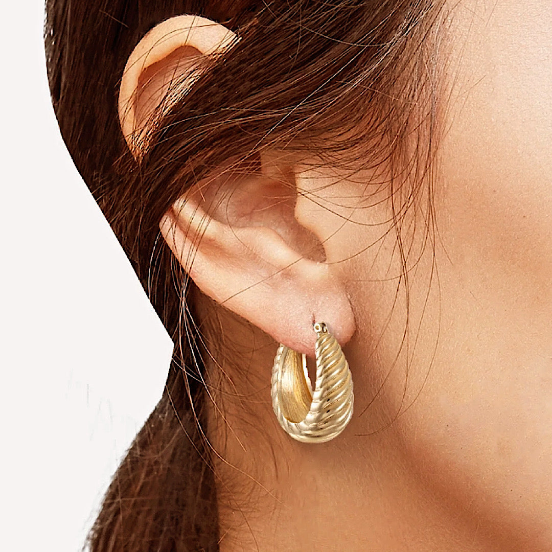 Gold hoop earring worn by a person with a neutral background