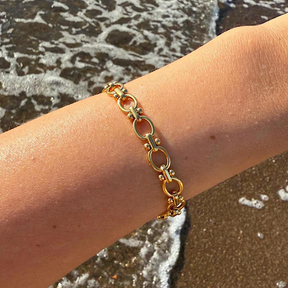Gold chain bracelet on a person's wrist with a beach background