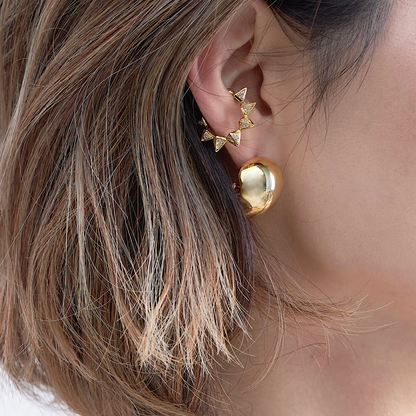 Close-up of an ear wearing gold earrings with a blurred background