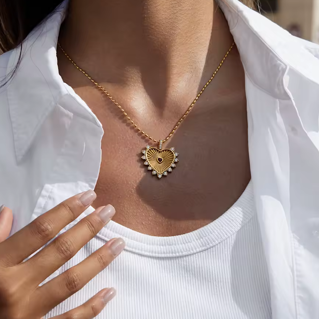 Gold heart-shaped necklace worn by a person in a white shirt.