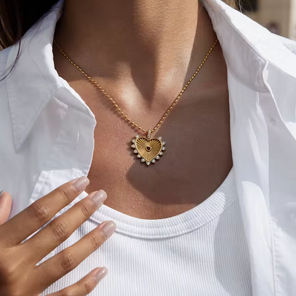 Gold heart-shaped necklace worn by a person in a white shirt.